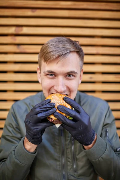 Hombre guapo comiendo hamburguesa uisy con carne de res en el fondo de madera. Concepto alimenticio . —  Fotos de Stock