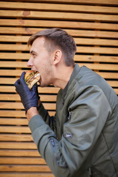 Hombre guapo comiendo hamburguesa uisy con carne de res en el fondo de madera. Concepto alimenticio . —  Fotos de Stock