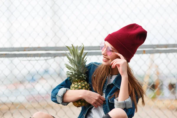 Mooi meisje zit met ananas buiten op de achtergrond van de natuur. — Stockfoto
