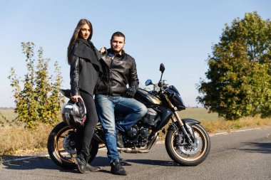 Bir kız bir motosiklet üzerinde oturan bir motosikletçi yanında duruyor