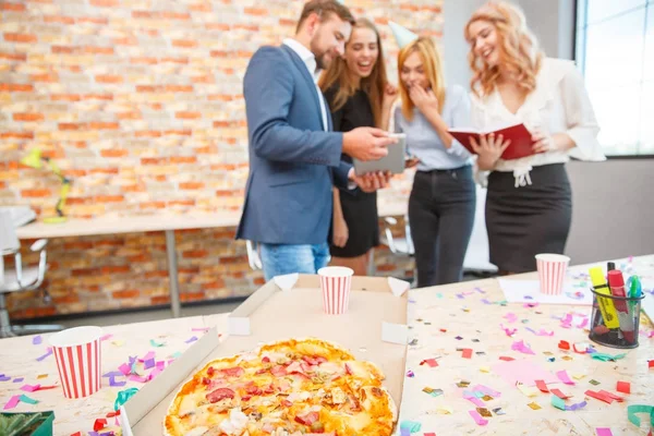 A company of young workers are browsing something on a tablet on a background of pizza closeup — Stock Photo, Image