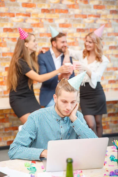 O empregado trabalha para um computador portátil no contexto da celebração da companhia de férias — Fotografia de Stock