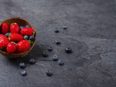Kase karanlık bir arka plan üzerinde bir yaban mersini ve tatlı taze çilek. Gıda kavramı.