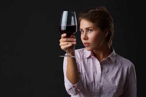 Hermosa chica con una copa de vino tinto sobre un fondo negro . — Foto de Stock