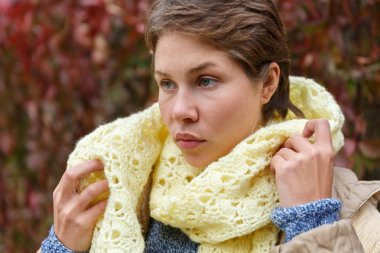 Portrait of a girl who straightens a white knitted scarf clipart