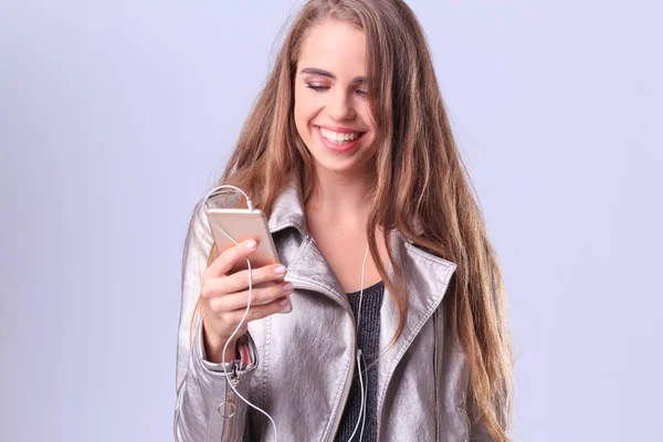 Una hermosa chica sobre un fondo gris escucha música desde su teléfono . — Foto de Stock