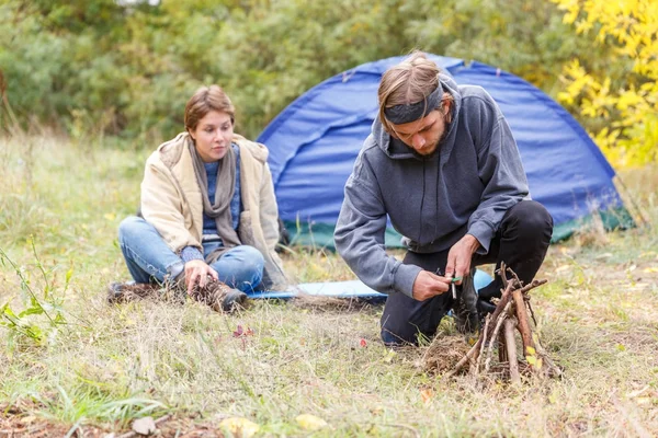 Couple in the forest. A man is kindling a fire. — Stock Photo, Image