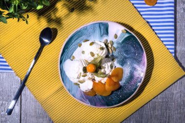 Canlandırıcı yaz ürünleri çok renkli bir dizi bir görünüm yukarıdan. Bir kase ile Besleyici fındık, Kuru Kayısı, yeşil yeşillik ve sarı kumaş arka plan üzerinde metal bir kaşık beyaz dondurma. 