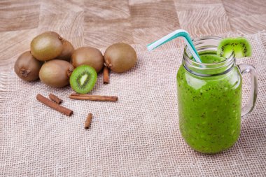 Bir büyük mason kavanoza renkli bir saman ve meyve ahşap arka plan üzerinde bir üstüne bir dilim ile olgun kivi organik içki dolu. Bir yığın bütün ve kesme kivi ve tarçın bir beyaz masa örtüsü üzerinde.