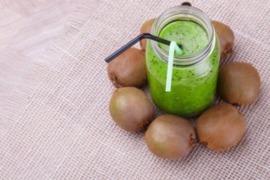 Bir görüntü yukarıdan bir kompozisyon bir taze yüzlü doğal kivi ile beyaz bir masa örtüsü ve hafif bir ahşap arka plan. Organik ve taze yeşil içecek payet ile. İçki yakınındaki bütün kivi.