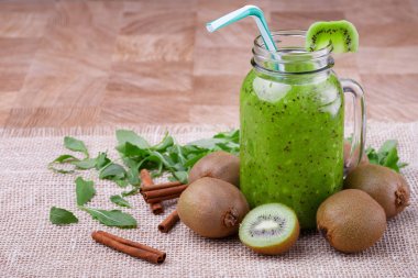 Sağlıklı kivi güler yüzlü bir renkli saman ve meyve ahşap arka plan üzerinde bir üst dilim bir mason kavanoza bir kompozisyon. Egzotik bütün ve kesme kivi, tarçın ve beyaz bir bez yapraklarda.