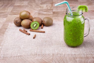 Bir büyük mason kavanoza bir renkli saman ve meyve ahşap arka plan üzerinde bir üst dilim ile olgun kivi gelen organik içecek dolu. Bir yığın bütün ve kesme kivi ve tarçın üzerinde hafif bir masa örtüsü.