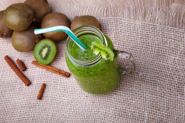 Renkli yüzlü kokteyl ve taze olgun kivi, kahverengi güzel kokulu tarçın hafif kumaş arka plan ile bir görünüm yukarıdan. Geniş bir mason kavanoza ekşi kivi içecek ile. Kopya alanı.