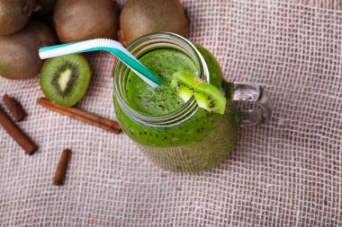 Renkli yüzlü kokteyl ve taze olgun kivi, kahverengi güzel kokulu tarçın hafif kumaş arka plan ile bir görünüm yukarıdan. Geniş bir mason kavanoza ekşi kivi içecek ile. Kopya alanı.