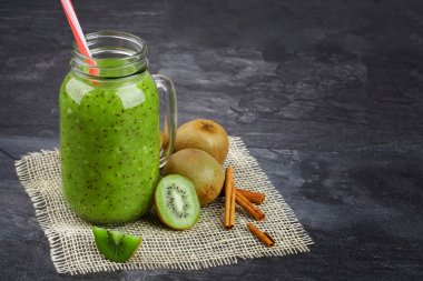 Bir mason kavanoza kivi yoğurt ve gri arka plan üzerinde doğal maddeler tam bir yakın çekim resim. Güzel yüzlü krem kumaş üzerinde egzotik kivi grubunun yanındaki. Yaz içecek. Kopya alanı.