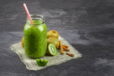 Bir close-up bir mason kavanoza kivi yoğurt ve gri arka plan üzerinde doğal maddeler dolu. Güzel yüzlü krem kumaş üzerinde egzotik kivi grubunun yanındaki. Yaz içecek. Kopya alanı.