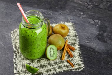 Yukarıdan bir görünümü temel bir mason kavanoza kivi yoğurt ve kumaş siyah bir arka plan üzerinde doğal maddeler. Kivi meyve yığını yanında dekoratif aromatik tarçın. Kopya alanı.