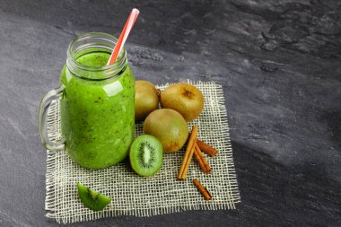 Gri taş zemin üzerine üstten görünüm yeşil kivi içecek. Renkli bir saman bir mason kavanoza bir kokteyl. Renkli kivi ve tarçın krem kumaş üzerinde kafes. Kopya alanı.