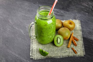 Gri taş zemin üzerine üstten görünüm yeşil kivi içecek. Renkli bir saman bir mason kavanoza bir kokteyl. Renkli kivi ve tarçın krem kumaş üzerinde kafes. Kopya alanı.