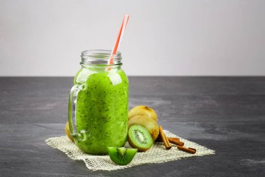 Bir close-up bir mason kavanoza kivi yoğurt ve gri arka plan üzerinde kumaş üzerinde doğal maddeler. Yeşil içecek ve yanındaki bir grup egzotik kivi kokulu tarçın. Kopya alanı.