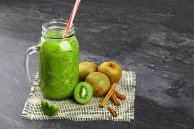 Yakın çekim bir serinletici kivi içecek gri taş arka plan. Renkli bir saman bir mason kavanoza bir kokteyl. Renkli kivi, tarçın sopa ve yanındaki soğuk bir içecek nane yaprakları. Kopya alanı.