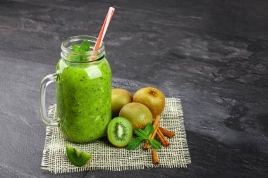 Yakın çekim bir serinletici kivi içecek gri taş arka plan. Renkli bir saman bir mason kavanoza bir kokteyl. Renkli kivi, tarçın sopa ve yanındaki soğuk bir içecek nane yaprakları. Kopya alanı.