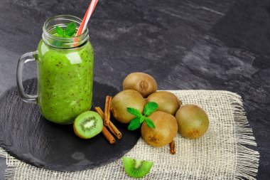 Bir bileşimi tropikal kivi, mason kavanoza kivi suyu, taze nane ve tarçın karanlık tablo arka plan üzerinde siyah bir tepsi dolu. Sağlıklı malzemelerle yaz içecekler için. Kopya alanı.