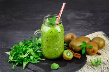 Bir close-up bir mason kavanoza kivi suyu ve siyah tablo arka plan üzerinde organik maddeler. Dekoratif ağaçlar ve tarçın olgun kivi yığını bir yanında. Kopya alanı. 