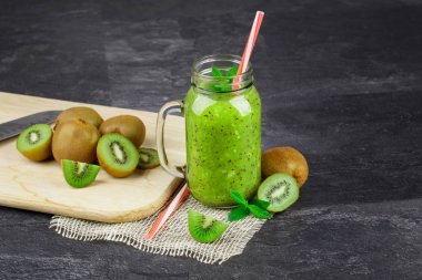 Kesme ve tüm kivi ve siyah bir arka plan üzerinde bir bıçak ile bir masa. Nane ve pipet ile soğuk ve ekşi kivi güler yüzlü büyük bir mason kavanoz. Yaz içecekler vitamin dolu. Kopya alanı. 