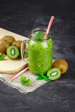 Renkli bir saman ile taze kivi güler yüzlü, uzun boylu bir mason kavanoza bir close-up. Hafif bir resepsiyon ve nane yaprakları bir taş tablo arka plan üzerine kıyılmış kivi. Yeşil besleyici kokteyller.