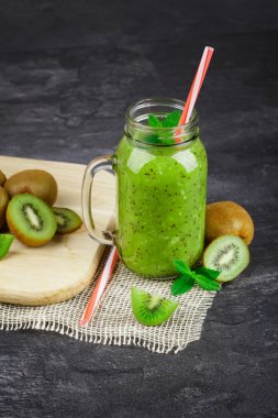 Kivi serinletici şeffaf bir mason kavanoza bir close-up bir saman ile sarsılıyor. Bir kesme Resepsiyon ve nane bir siyah tablo arka plan üzerine kıyılmış kivi. Yeşil suları besinlerin tam.