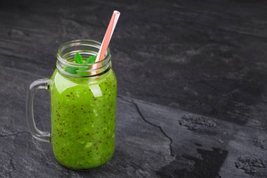 Şeffaf bir mason kavanoza kivi güler yüzlü ile. Bir cam şişe siyah tablo arka plan üzerinde yeşil milkshake doymuş. Nane ve kırmızı bir saman ile renkli milkshake. Kopya alanı. 