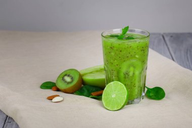 Ferahlatıcı bir kivi içecek bir bej tablo-kumaş ve ahşap masa close-up. Bir kokteyl gri bir arka plan üzerine taze meyve ile. Renkli kivi, fındık, kireç ve elma vitamin dolu. Kopya alanı.