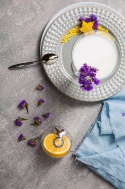 Alkolsüz içecek ile bir plaka üzerinde bir görünüm yukarıdan. Bir bardak hafif gri arka plan üzerinde carambola ve mor çiçekler ile güler yüzlü. Kesilmiş limon ve bir kaşık beyaz muzlu süt.