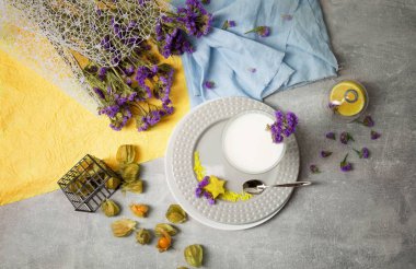 Doğal bir milkshake ve tropikal meyve gri bir arka plan üzerinde bir görünüm yukarıdan. Bir tatlı bir dekoratif çiçek buketi, physalis ve gri bir kaşık ile yuvarlak tabak. Restoran tatlılar.