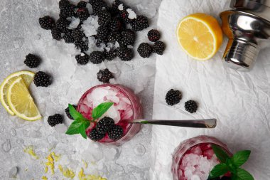 Glasse buzlu içecek nane ve böğürtlen üzerinde gri bir arka plan ile bir kompozisyon bir görünüm yukarıdan. Olgun, taze böğürtlen, parlak nane ve soğuk bir içecek için kesilmiş bir sarı limon.