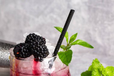 Yaz taze kokteyl özlü böğürtlen, buz küpleri ile yakın çekim yeşil gri hafif bir arka plan üzerinde siyah nemli içme saman ve nane bırakır. Yaz içecekler.