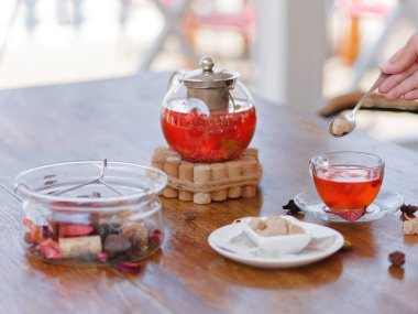 Bir kadının elini bir gümüş kaşık şeker ve Karpuzu Çay ile ahşap bir masa ve arka plan bulanık tutuyor. Bir çaydanlık çilek içecek dolu bir masa üzerine kuş üzümü ile. Sağlıklı içecek.