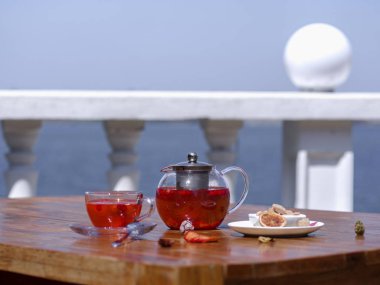 Bir güzel parlak kompozisyonu bir çaydanlık kahverengi ahşap bir masa üzerinde organik berry içecek dolu. Şeker, su ısıtıcısı ve bir fincan taze yabani çilek deniz arka plan üzerinde kahverengi küpleri ile bir tabak.