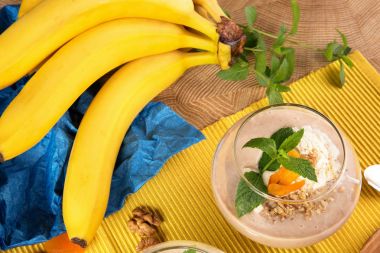 Bir tatlı cam dolu meyve yüzlü dondurma, muz, Kuru Kayısı ve bir şube ve nane yaprakları ile parlak sarı bir arka plan üzerinde muz close-up. Muz milkshake meyve ile.