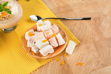 Fantastik Türk lokumu bir seramik tabak kahverengi ahşap masa lambası arka plan üzerinde bir yığın. Meyve, pudra şekeri ve bir içecek ile rahat lokum. Uzun metal kaşık ile egzotik bir tatlı.