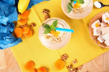 Rahat lokum, metalik bir kaşık, parlak Kuru Kayısı, ceviz, muz bir tabak ile üst görünümden bir tablo kokteyller ile bir bardak rendelenmiş ceviz ve renkli bir arka plan üzerine nane yaprakları.