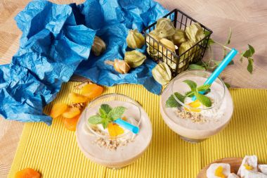 Kuru Kayısı, ceviz, nane, physalis, sarı ve mavi peçeteler, lokum renkli bir arka plan üzerine bir tabak yeşil yaprakları ile süslenmiş kokteyller iki bardak ile ahşap bir masa.