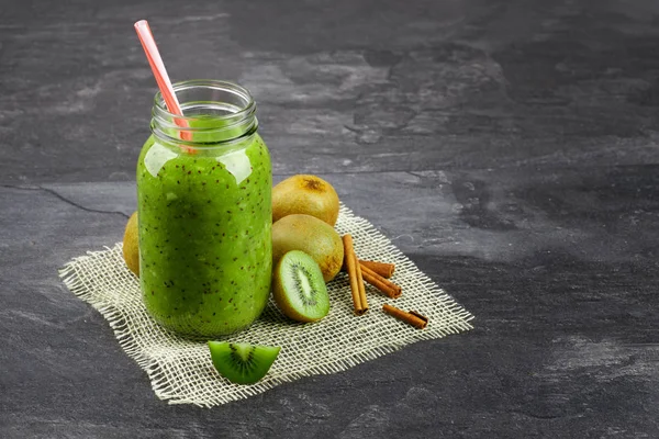 Bir close-up bir mason kavanoza kivi yoğurt ve gri arka plan üzerinde doğal maddeler dolu. Güzel yüzlü krem kumaş üzerinde egzotik kivi grubunun yanındaki. Yaz içecek. Kopya alanı.
