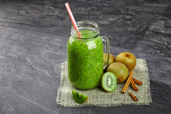 Gri taş zemin üzerine yeşil kivi içecek close-up. Renkli bir saman bir mason kavanoza bir kokteyl. Renkli kivi ve tarçın yanında soğuk bir içecek. Kopya alanı.
