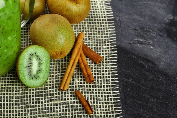 Close-up of a group of kiwis on a fabric mesh. Exotic refreshing fruits with cinnamon sticks on a black background. Healthful fruits and herbs ingredients. Copy space.