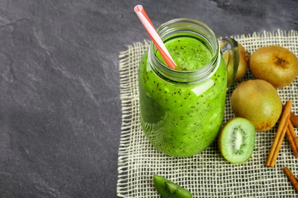 A view from above on a jar filled with a bright green healthful smoothie with a striped straw. A healthy, refreshing and exotic cocktail full of vitamins and whole kiwis on a gray table background.