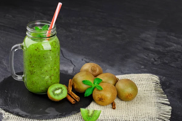 Grup çiğ kivi, mason kavanoza yeşil milkshake, baharatlı tarçın taş tablo arka plan üzerinde beyaz kumaş üzerinde dolu renkli bir dizi. Vegan içecekler için sulu malzemeler. Kopya alanı.