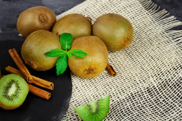 Close-up of a group of five kiwis on a white fabric. Exotic refreshing fruits with peppermint and cinnamon on a black background. Healthful fruits and herbs ingredients.