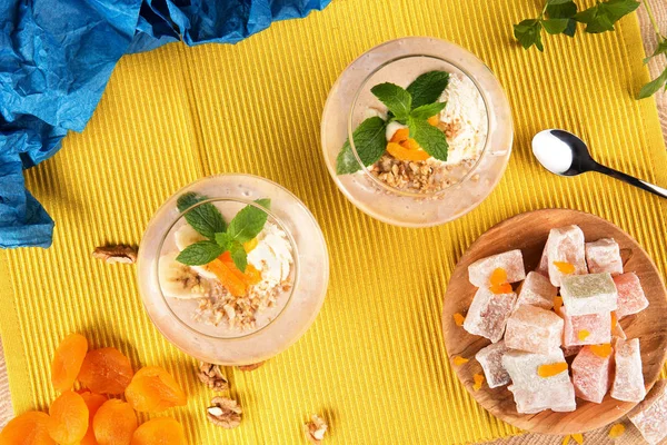 Top view of two banana smoothies in a huge glasses with Turkish Delight, dried apricots, walnuts and spoon on multi-colored background. Healthy smoothie with sweets. and fruits.